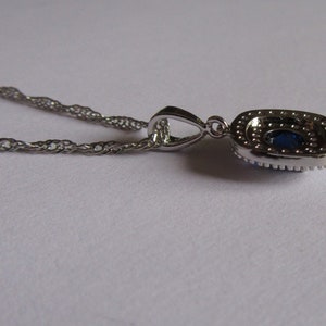 May include: A silver chain necklace with a pendant featuring a large blue oval gemstone surrounded by smaller clear gemstones.