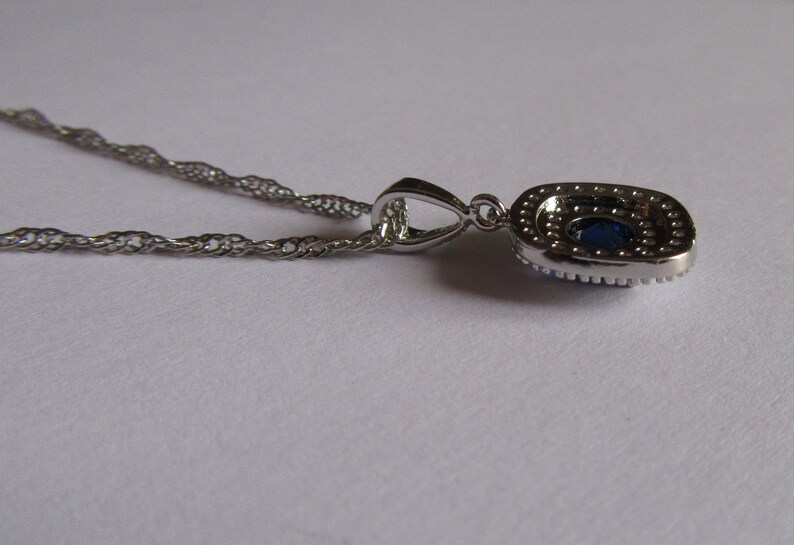 May include: A silver chain necklace with a pendant featuring a large blue oval gemstone surrounded by smaller clear gemstones.