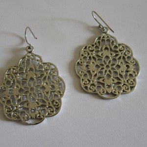 May include: A pair of silver filigree earrings with a delicate, intricate design. The earrings are round and have a floral pattern.