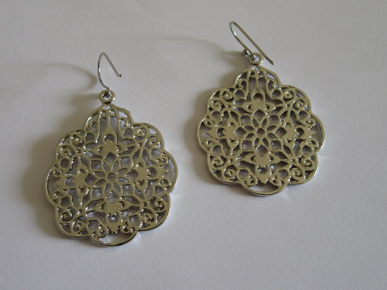 May include: A pair of silver filigree earrings with a delicate, intricate design. The earrings are round and have a floral pattern.