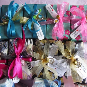 May include: Assortment of small gift boxes wrapped in various patterned papers and tied with colorful ribbons. The boxes have tags attached with the text "Handmade with love" and "Thank you".