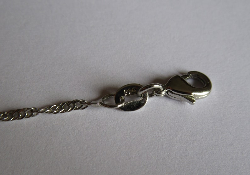 May include: A silver chain necklace with a lobster clasp closure. The chain is a delicate, twisted design.