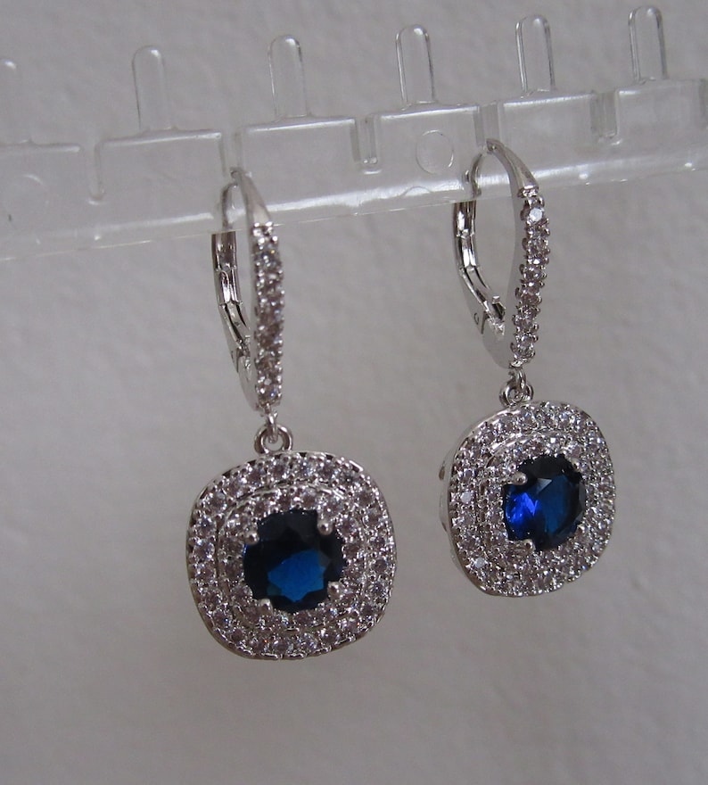 May include: A pair of silver dangle earrings with a blue gemstone surrounded by clear cubic zirconia stones.