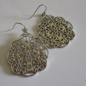 May include: A pair of silver filigree drop earrings with a delicate, intricate design. The earrings are lightweight and have a classic, elegant look.