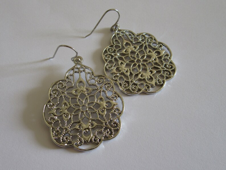 May include: A pair of silver filigree drop earrings with a delicate, intricate design. The earrings are lightweight and have a classic, elegant look.