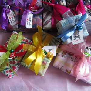May include: An assortment of small gift boxes wrapped in colourful patterned paper with ribbons and tags. The boxes are tied with various colours of ribbon, including pink, blue, yellow, and green. The tags have handwritten messages, including "Handmade with love" and "Thank you".