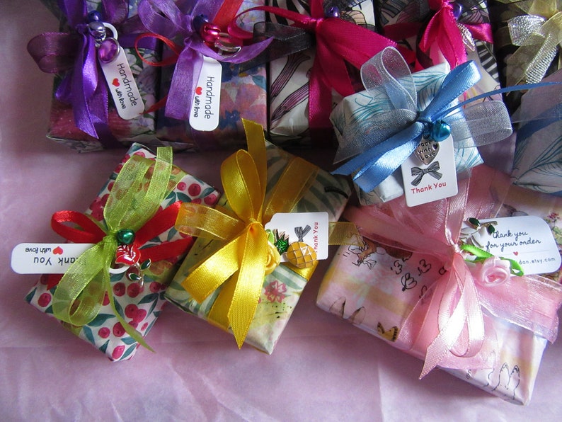 May include: An assortment of small gift boxes wrapped in colourful patterned paper with ribbons and tags. The boxes are tied with various colours of ribbon, including pink, blue, yellow, and green. The tags have handwritten messages, including "Handmade with love" and "Thank you".