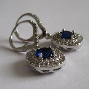 May include: A pair of silver dangle earrings with a large blue gemstone surrounded by smaller clear gemstones.