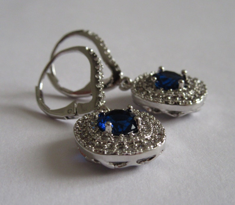 May include: A pair of silver dangle earrings with a large blue gemstone surrounded by smaller clear gemstones.