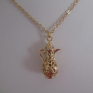 Könnte beinhalten: Eine goldfarbene Halskette mit einem detaillierten filigranen Teekannenanhänger. Der Anhänger hat einen klaren Kristall-Akzent auf dem Deckel.