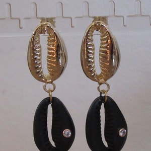 May include: Gold and black shell-shaped earrings with a small rhinestone accent. The earrings are dangling and have a simple design.