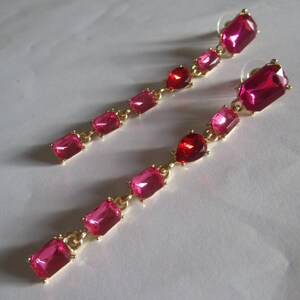 May include: A pair of long, dangling earrings with a gold chain and five pink rectangular gemstones.