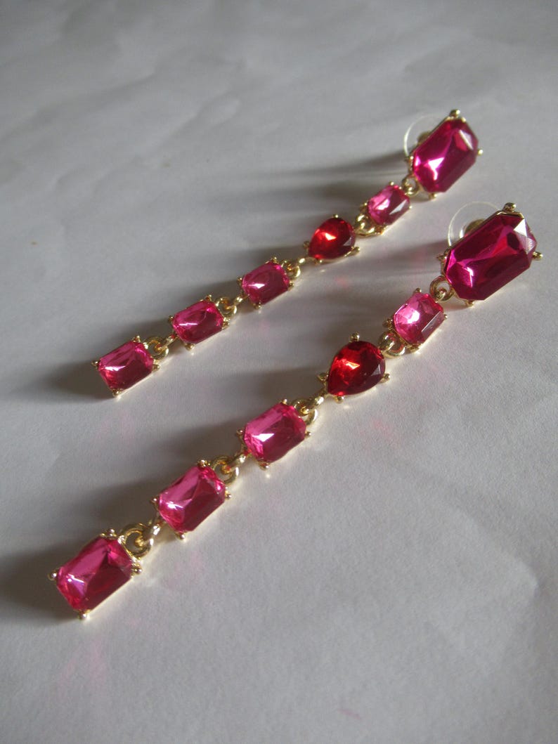 May include: A pair of long, dangling earrings with a gold chain and five pink rectangular gemstones.