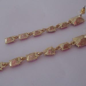 May include: A pair of long, gold earrings with pink rectangular stones. The earrings have a dangling design with multiple stones.