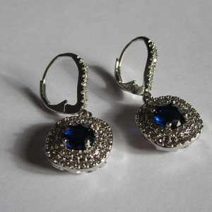 May include: A pair of silver dangle earrings with a blue gemstone surrounded by smaller clear gemstones.