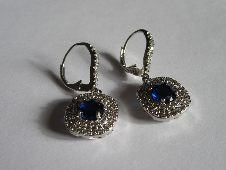 May include: A pair of silver dangle earrings with a blue gemstone surrounded by smaller clear gemstones.