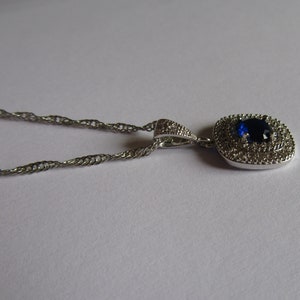 May include: A silver chain necklace with a pendant featuring a large blue gemstone surrounded by smaller clear gemstones.