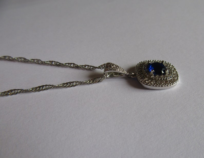 May include: A silver chain necklace with a pendant featuring a large blue gemstone surrounded by smaller clear gemstones.