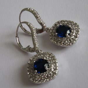 May include: A pair of silver dangle earrings with a blue gemstone surrounded by smaller clear gemstones.