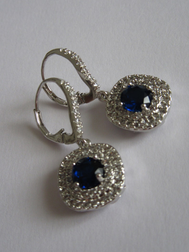 May include: A pair of silver dangle earrings with a blue gemstone surrounded by smaller clear gemstones.
