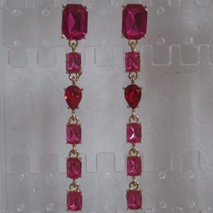 May include: A pair of long, dangling earrings with multiple pink rectangular and teardrop-shaped stones. The earrings are gold-toned.