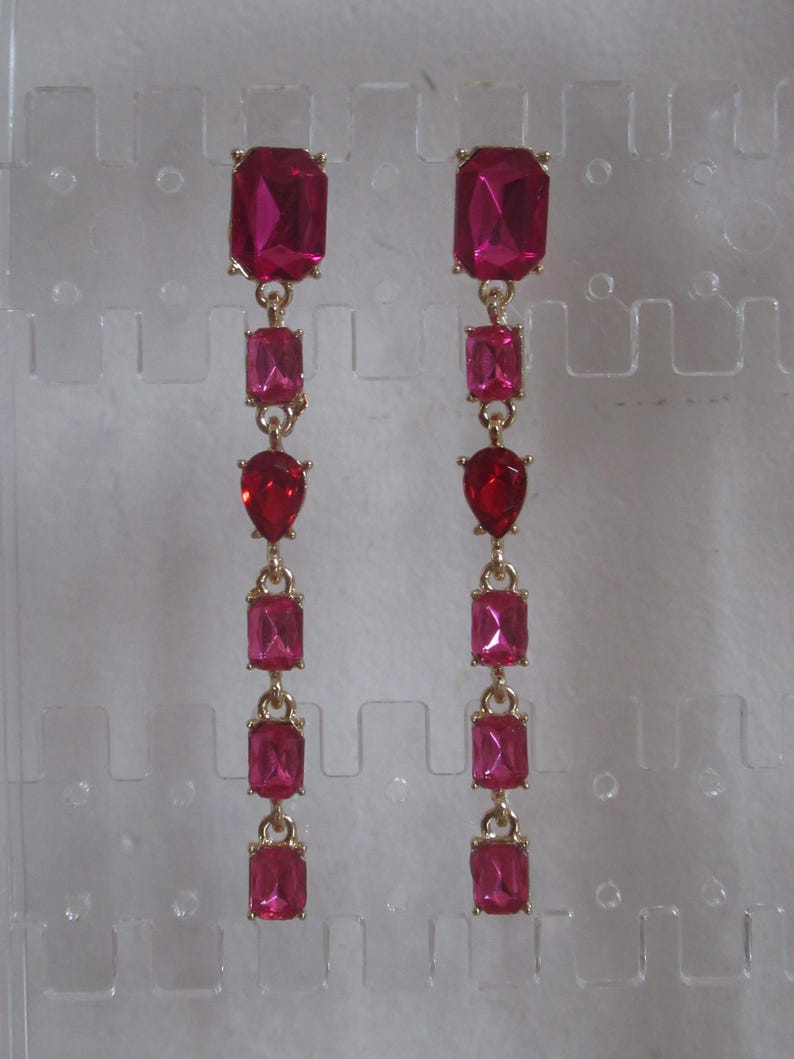 May include: A pair of long, dangling earrings with multiple pink rectangular and teardrop-shaped stones. The earrings are gold-toned.
