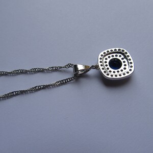 May include: A silver chain necklace with a square pendant featuring a blue gemstone surrounded by smaller clear stones.