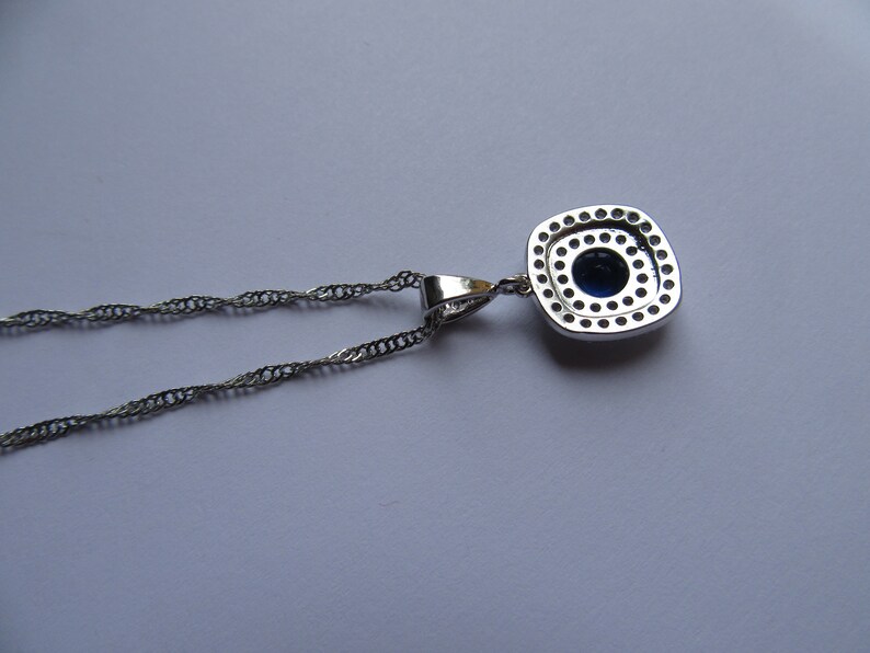 May include: A silver chain necklace with a square pendant featuring a blue gemstone surrounded by smaller clear stones.
