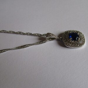 May include: A silver chain necklace with a pendant featuring a large blue gemstone surrounded by smaller clear gemstones.