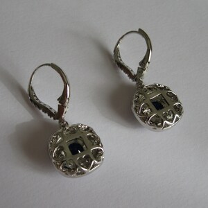May include: A pair of silver dangle earrings with a round, openwork design featuring a dark blue gemstone in the center.