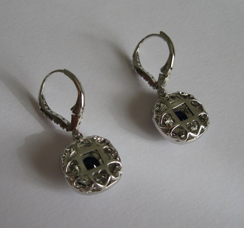 May include: A pair of silver dangle earrings with a round, openwork design featuring a dark blue gemstone in the center.