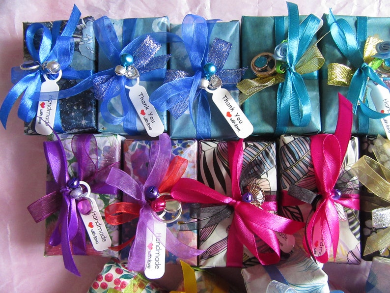 May include: Assortment of small gift boxes wrapped in various colorful patterned papers and tied with ribbons. The boxes have tags that say "Handmade with love" and "Thank you with love".