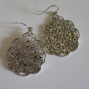 May include: A pair of silver filigree earrings with a delicate floral design. The earrings are lightweight and have a dangling style.