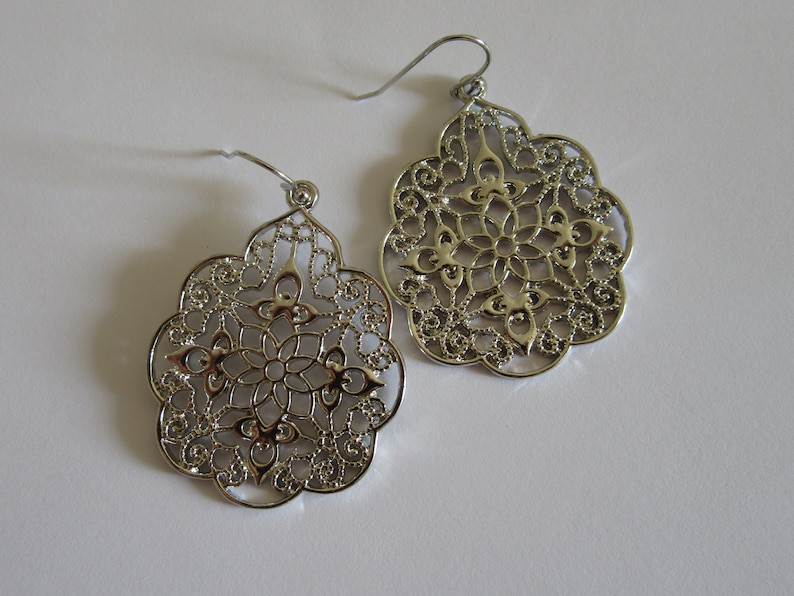 May include: A pair of silver filigree earrings with a delicate floral design. The earrings are lightweight and have a dangling style.