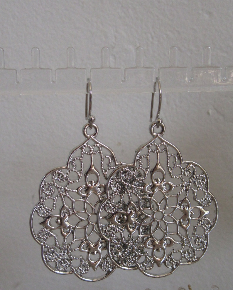 May include: A pair of silver filigree earrings with a delicate, intricate design. The earrings are shaped like a flower with a circular centre and multiple layers of delicate metalwork.