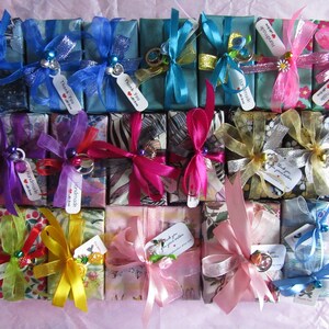 May include: A collection of small, wrapped gift boxes with various colorful patterned paper, ribbons, and bows. The boxes are tied with different colored ribbons, including blue, pink, yellow, purple, and green. Some boxes have small charms or embellishments attached to them. The boxes are arranged in a grid pattern on a pink surface. The boxes are all approximately the same size and shape.