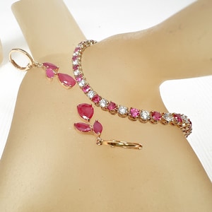 Puede incluir: Un conjunto de pulsera y pendientes de tono dorado con piedras rosas y blancas. La pulsera es de estilo tenis con piedras redondas rosas y blancas alternadas. Los pendientes son de estilo colgante con piedras rosas en forma de pera.