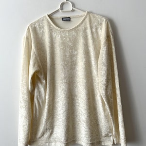 Op de afbeelding: Een crèmekleurig longsleeve shirt gemaakt van een zachte, fluweelachtige stof. Het shirt heeft een ronde hals en een losse pasvorm.