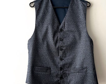 May include: A dark gray patterned vest with a black lining and five black buttons. The vest has two pockets on the front.