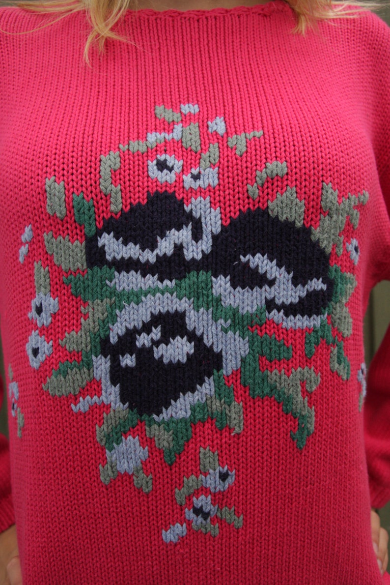 May include: A red knitted sweater with a colorful geometric design. The design features a black, green, and gray pattern.