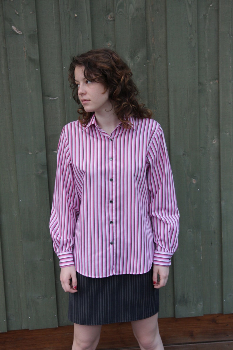 Puede incluir: Una mujer con una camisa de manga larga a rayas rosa y blancas y una falda negra de rayas finas.