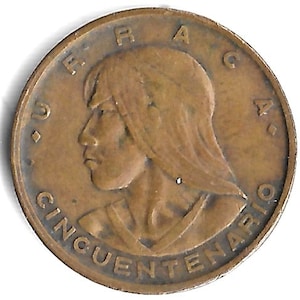 May include: A bronze coin featuring a profile of a person with long hair. The coin has the words "CINCUENTENARIO" and "VERAC" inscribed around the edges. The coin is circular and has a slightly worn appearance.