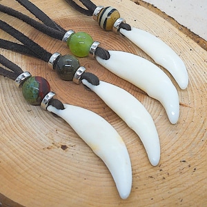 Pode incluir: Quatro colares com pingentes de dentes brancos e contas de pedras preciosas de diferentes cores. Os colares são feitos com cordão de couro marrom e detalhes em metal prateado.