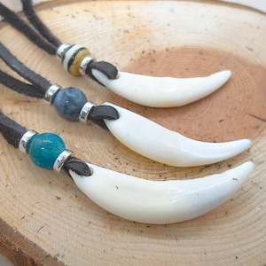 Op de afbeelding: Drie leren kettingen met witte tand hangers en blauwe en bruine kralen.