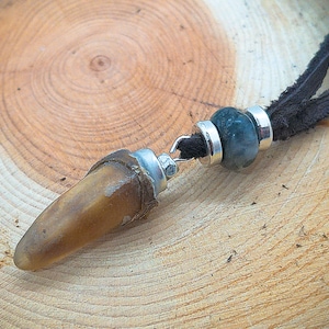 Puede incluir: Un colgante de diente marrón en un cordón de cuero negro con un cierre plateado y una cuenta de ágata verde.