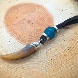 May include: A necklace with a brown tooth pendant and a teal blue glass bead. The necklace is made of black suede cord.