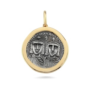 May include: A gold pendant with a silver coin-like centre. The centre features two figures with crowns and text around the edge. The pendant has a gold bail for a chain.