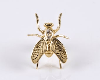 May include: A gold-toned fly brooch with a clear rhinestone on its body.