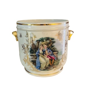 May include: A white ceramic planter with gold accents and a painted scene of a couple sitting on a bench in a garden. The planter has two gold handles.