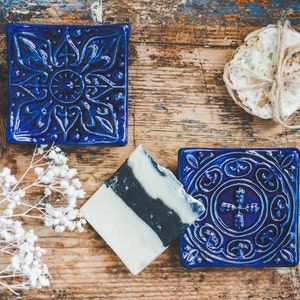 Puede incluir: Dos jaboneras de cerámica azul con intrincados diseños florales. Una barra de jabón blanco y negro descansa sobre una de las jaboneras.